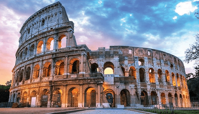 The Colosseum in Rome at sunset, with warm golden light reflecting off the ancient stone arches under a colorful evening sky.