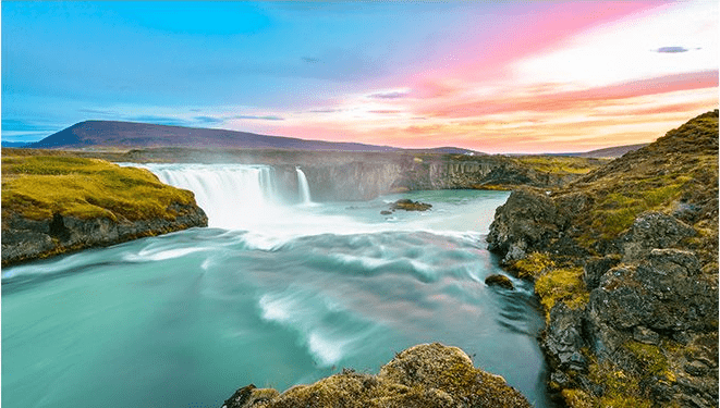 Waterfall cascading through the Icelandic landscape beneath a colorful sunset sky.