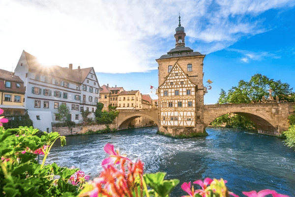 Historic half-timbered building standing in the middle of a river beneath a stone bridge in a picturesque European town.