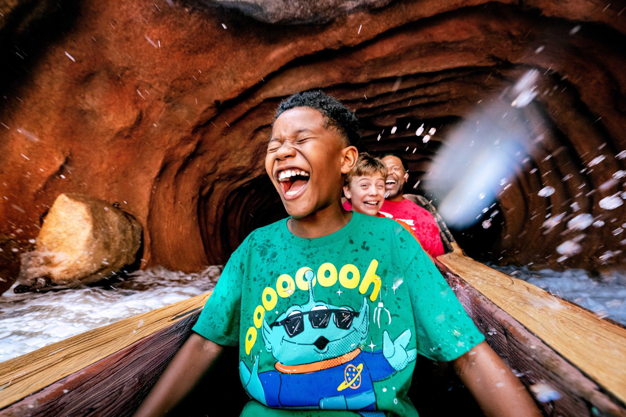 Child riding a log flume water ride as a large splash erupts around the boat, creating an exciting theme park adventure.